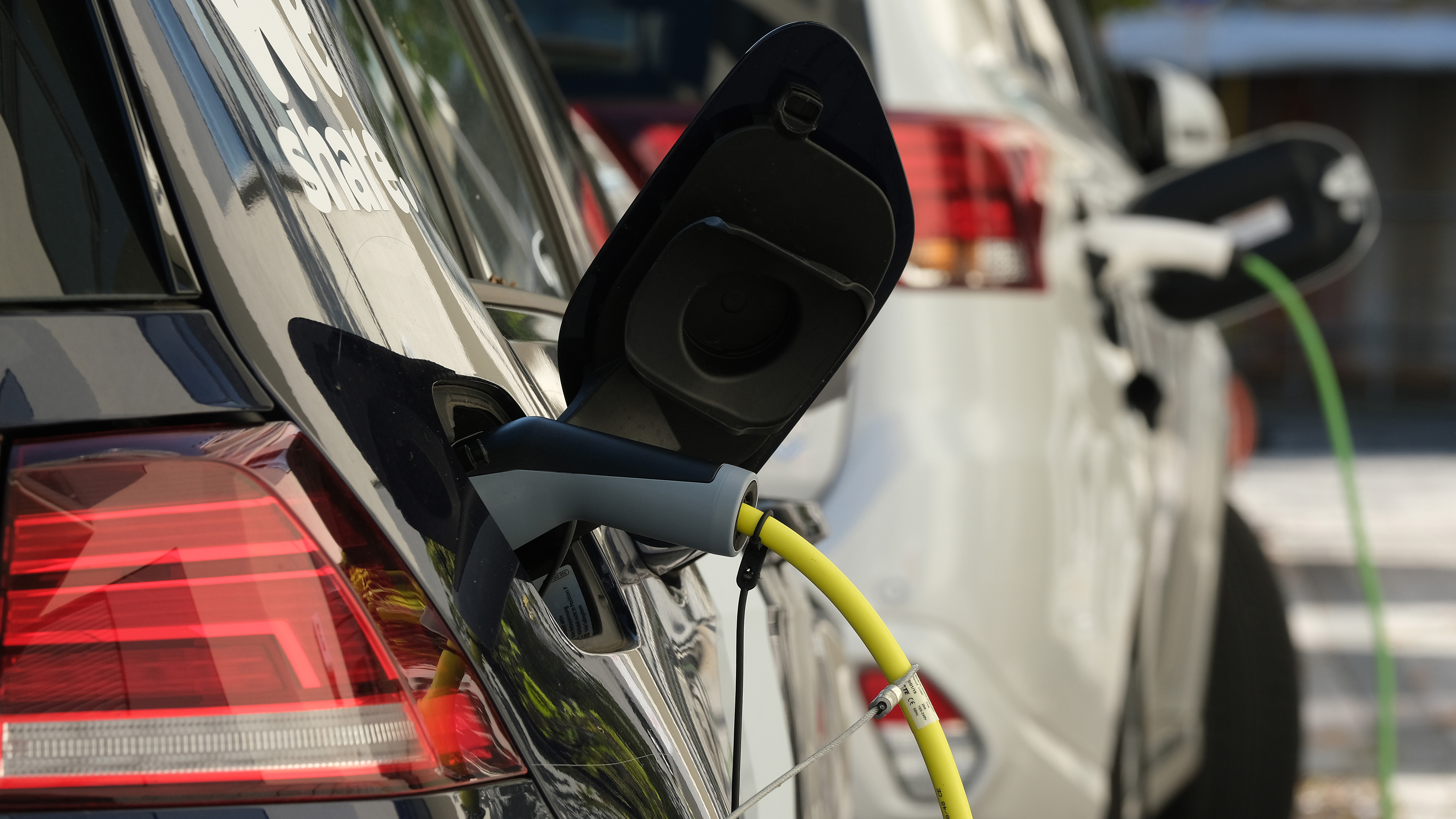 An electric car is seen charging with a plug-in hybrid car charging in the background.