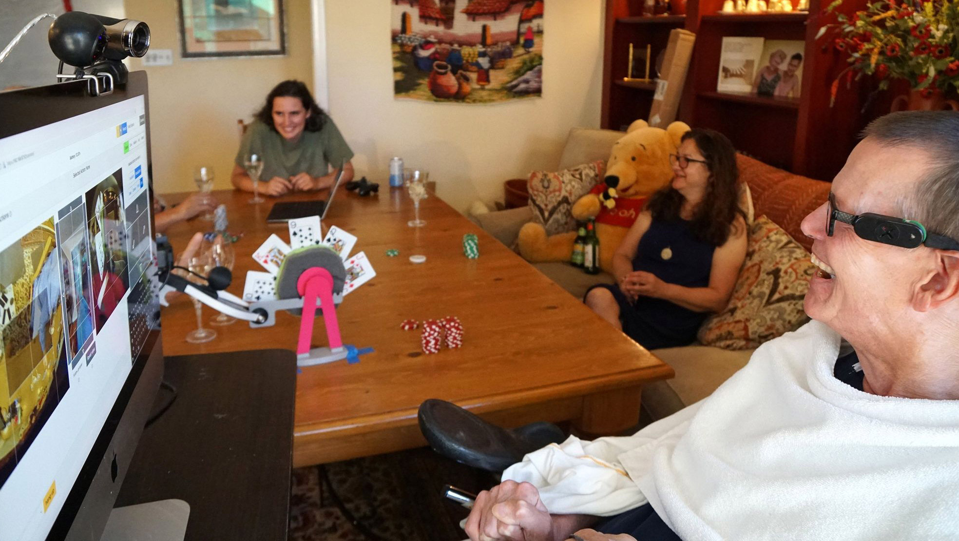 Evans in the foreground with computer screen.  A table with playing cards separates him from two other people in the room