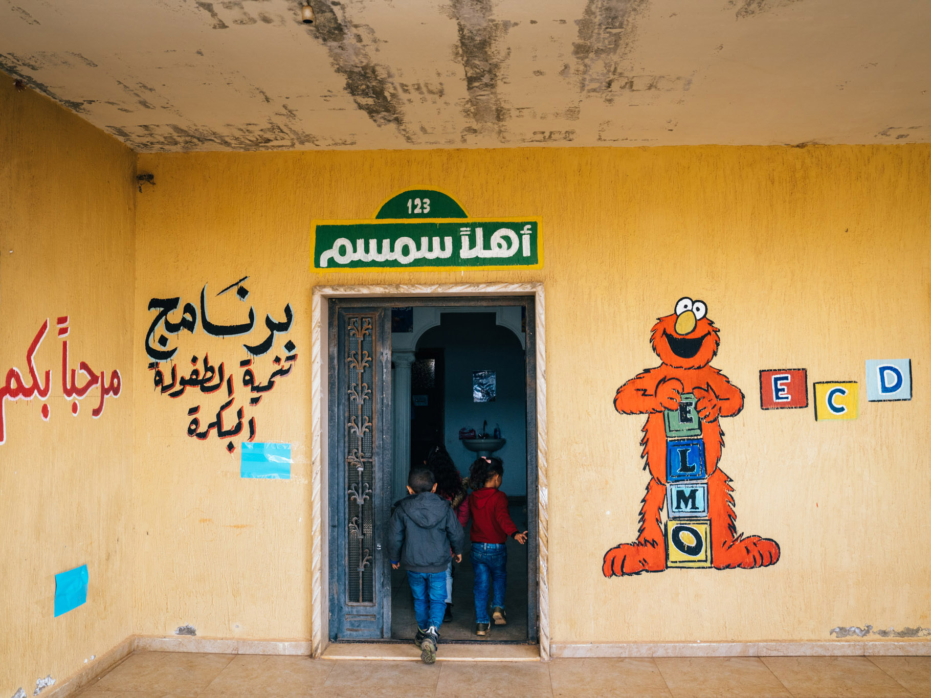 two children entering a door next to a mural of Elmo with ABC blocks